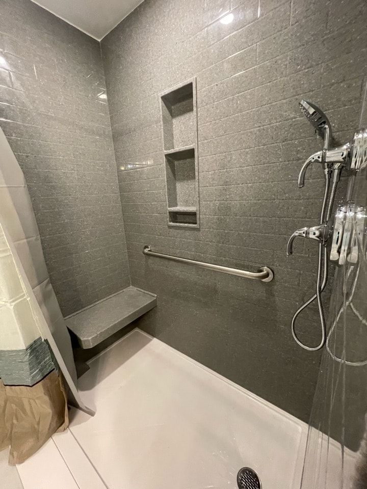 Gray-tiled accessible shower with a bench, grab bar, built-in shelving, and a handheld showerhead.