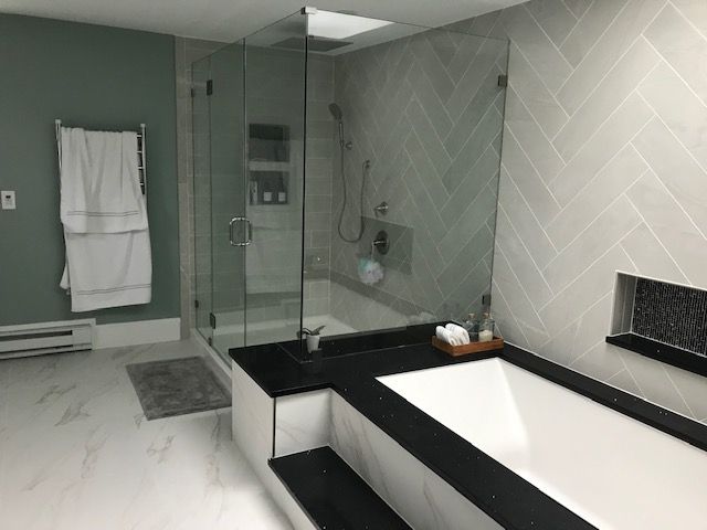 Modern bathroom with glass shower, soaking tub, and herringbone tile. Green wall, black countertop, white floor.