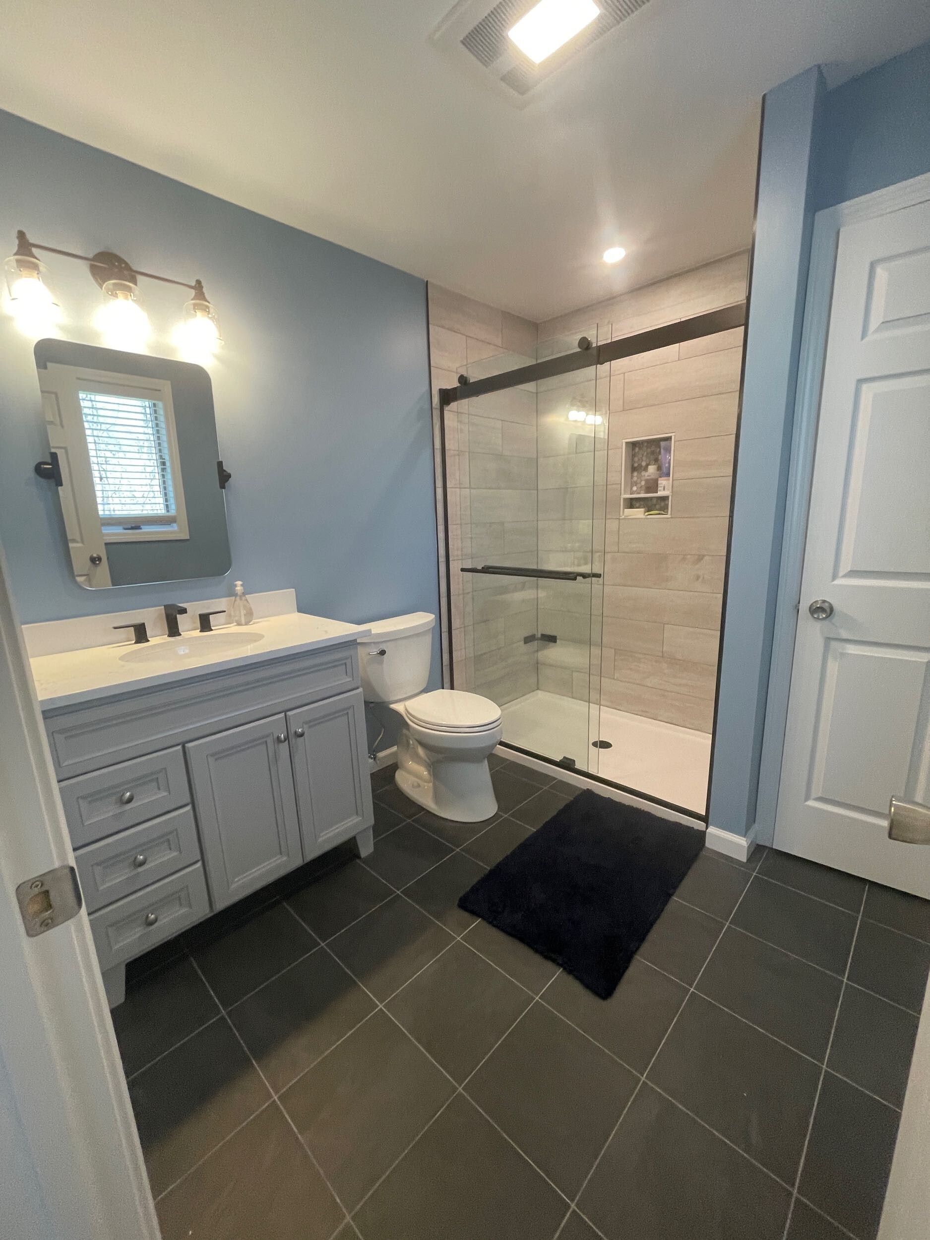 Bathroom with a blue wall, gray vanity, toilet, glass shower, and dark gray tile floor.