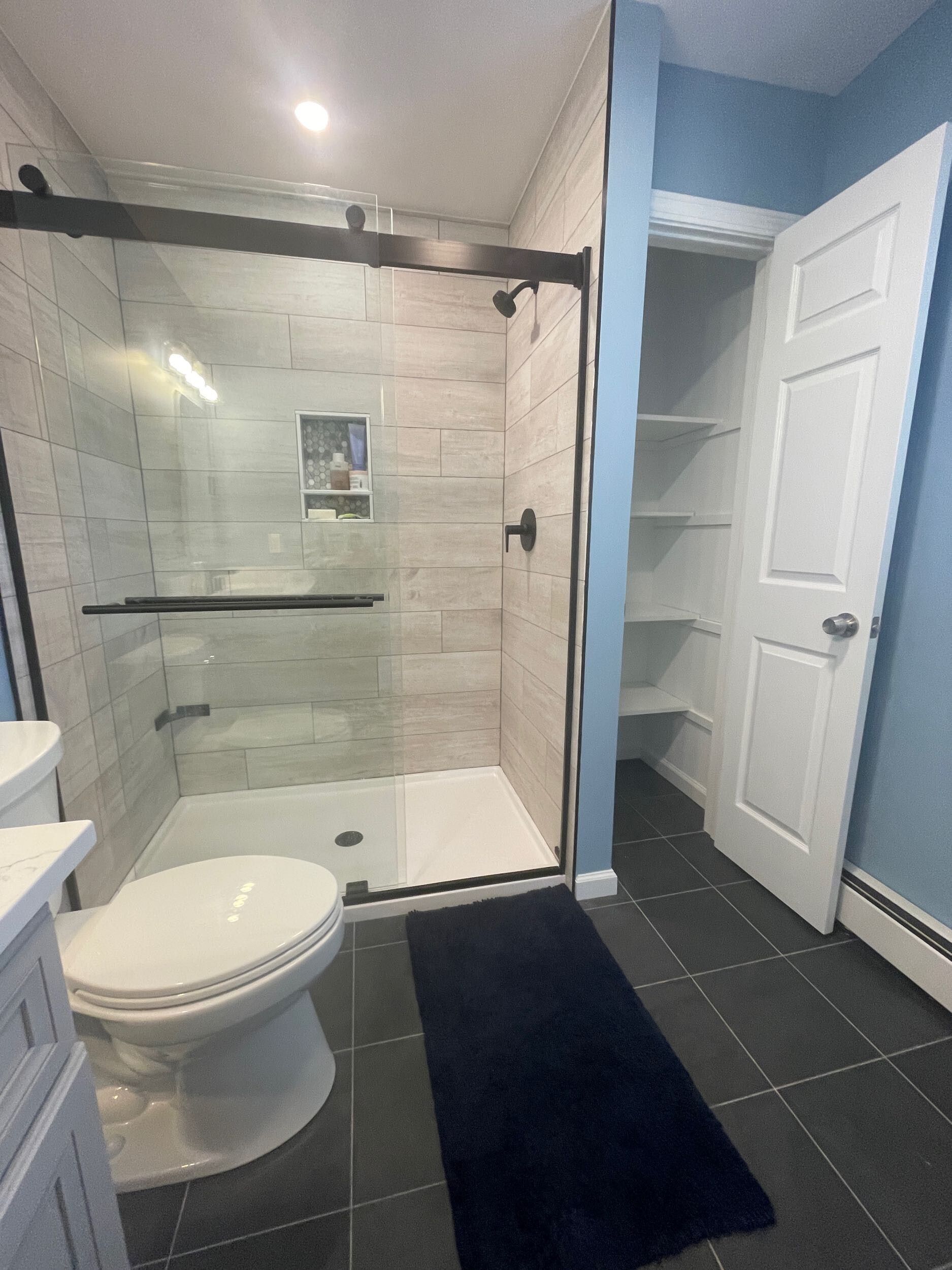 Modern bathroom with a glass shower, toilet, and storage closet.