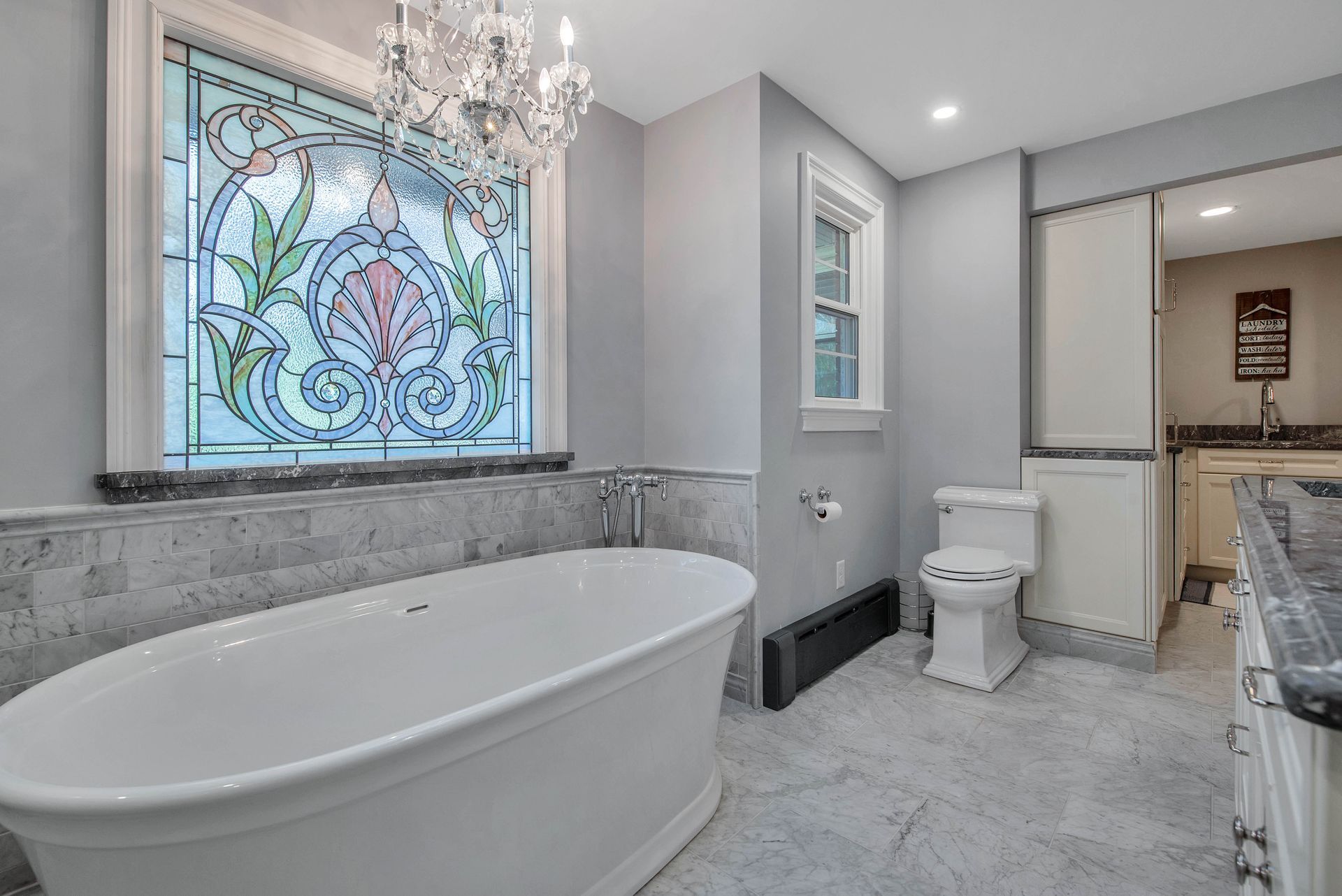 Bathroom with white tub, stained glass window, and gray walls and floor.