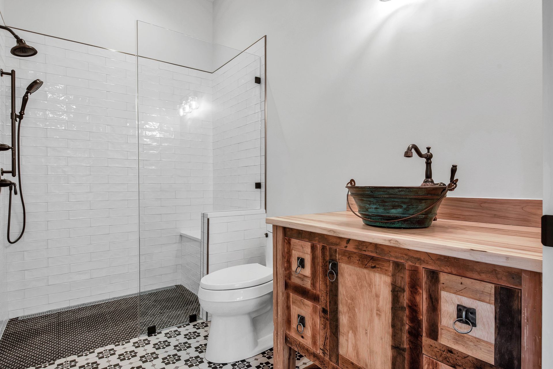 Bathroom with white tile shower, wooden vanity, and patterned floor.