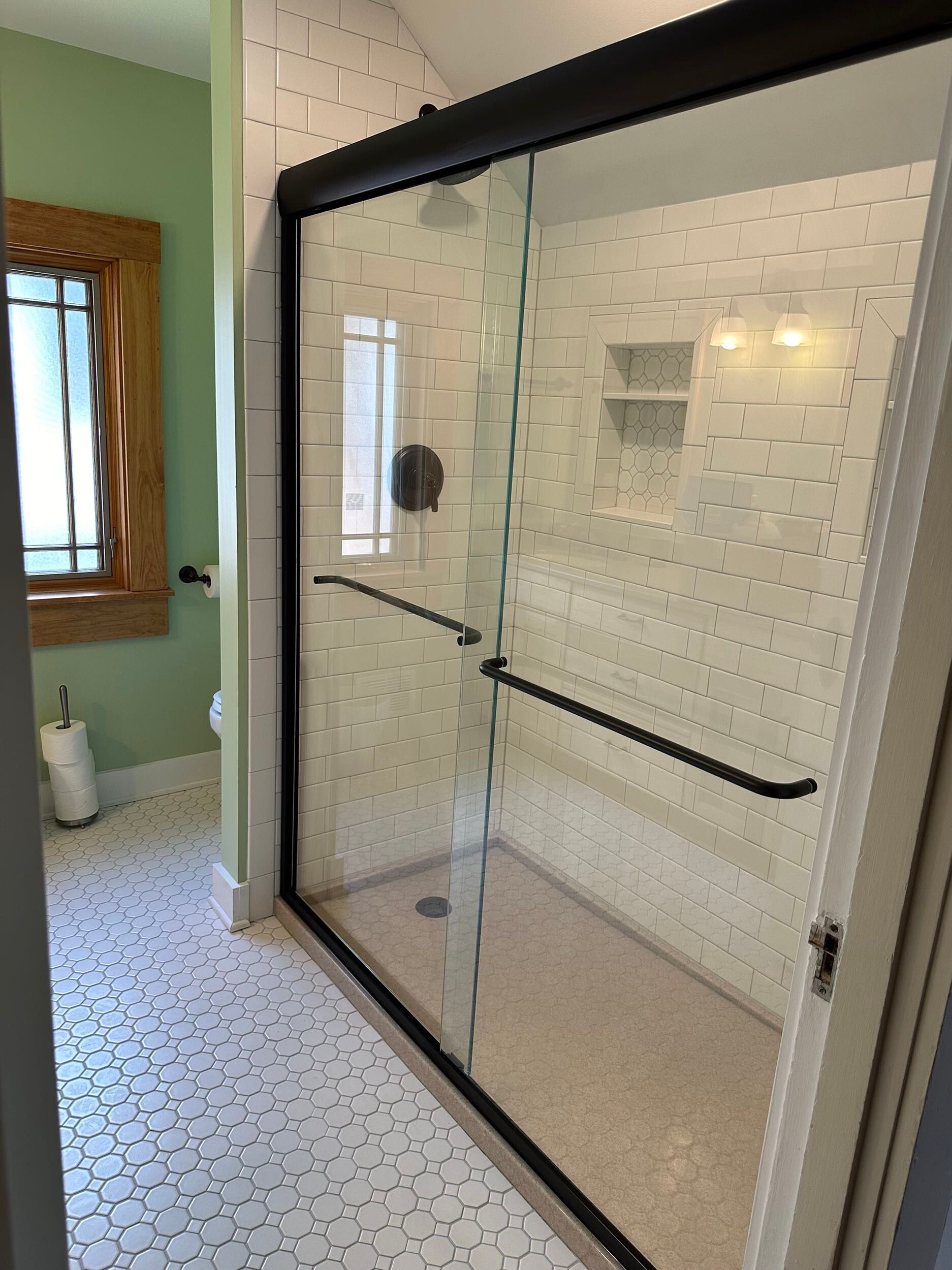 Bathroom with a clear glass shower, white honeycomb tile, and green walls.