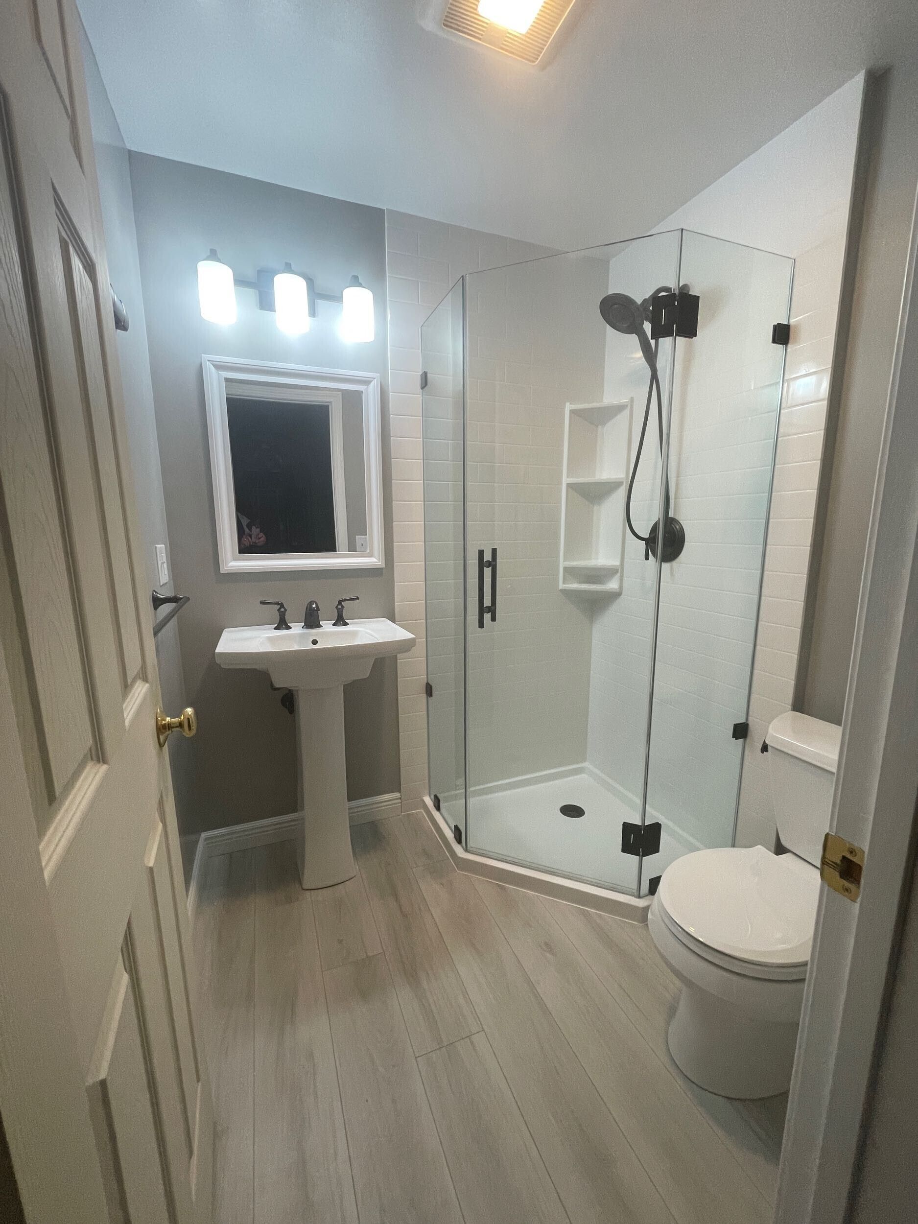 Bathroom with a pedestal sink, shower with glass door, and toilet; gray and white color scheme.