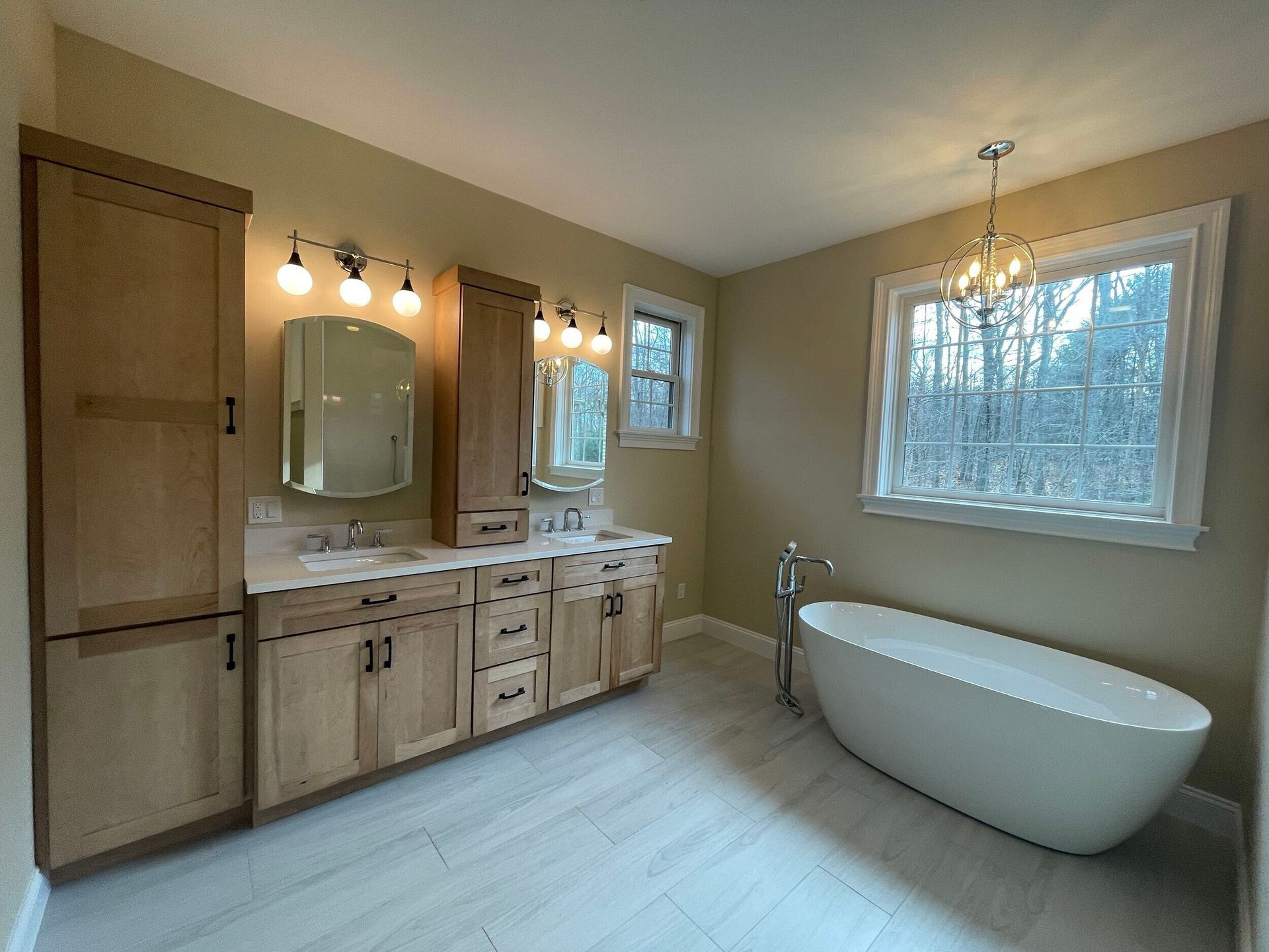 Spacious beige bathroom with wooden cabinets, double sink, bathtub, and large window.