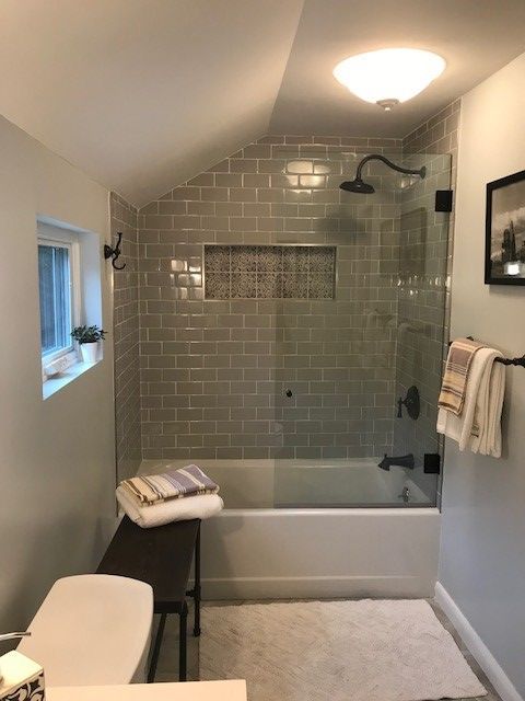 Bathroom with gray tile shower, glass door, tub, towels, and bench.