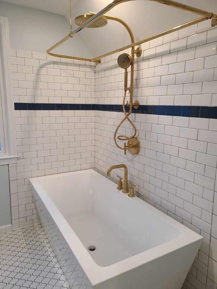 White bathtub with gold fixtures, white tiled walls with blue accent, and a gold shower rod.
