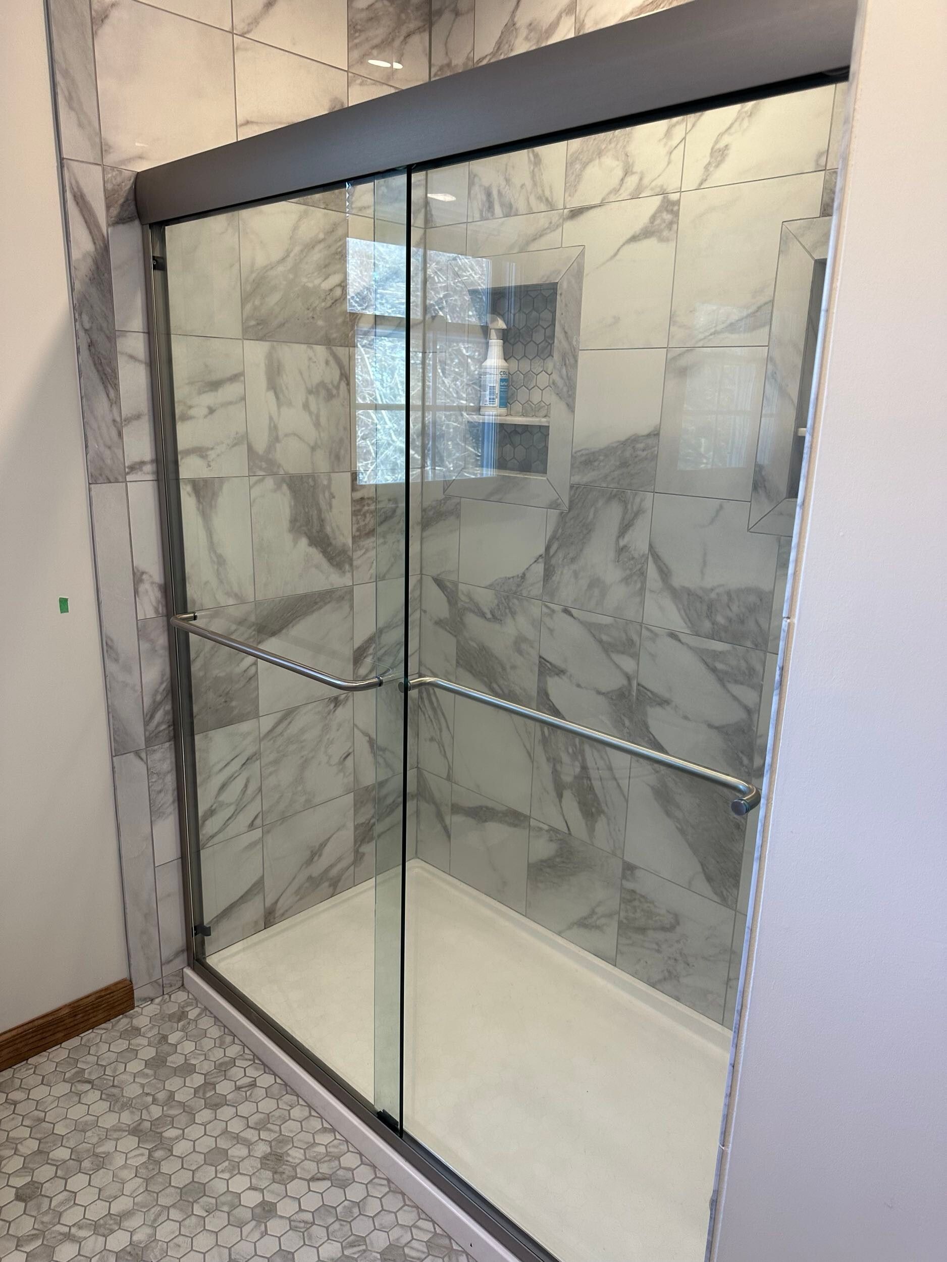 Glass shower enclosure with gray marble tile and a white base.