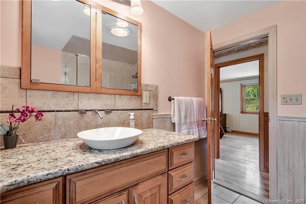 Bathroom with wooden cabinets, granite countertop, and vessel sink. Soft pink walls, doorway to a hallway.