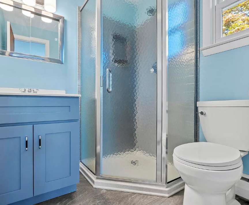 Blue bathroom with a corner shower, toilet, and vanity.