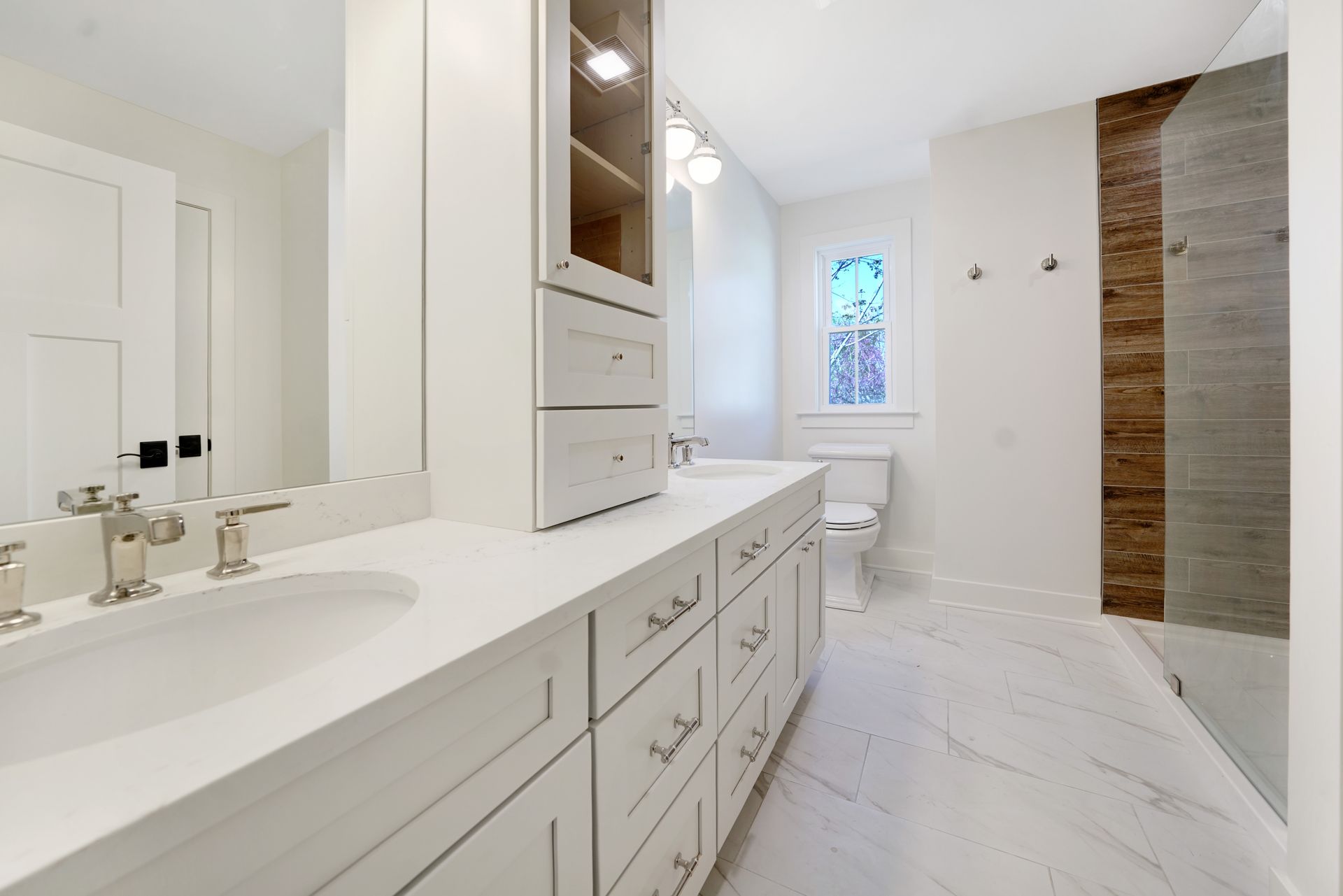 Bathroom with white cabinets, marble floors, and a glass shower.