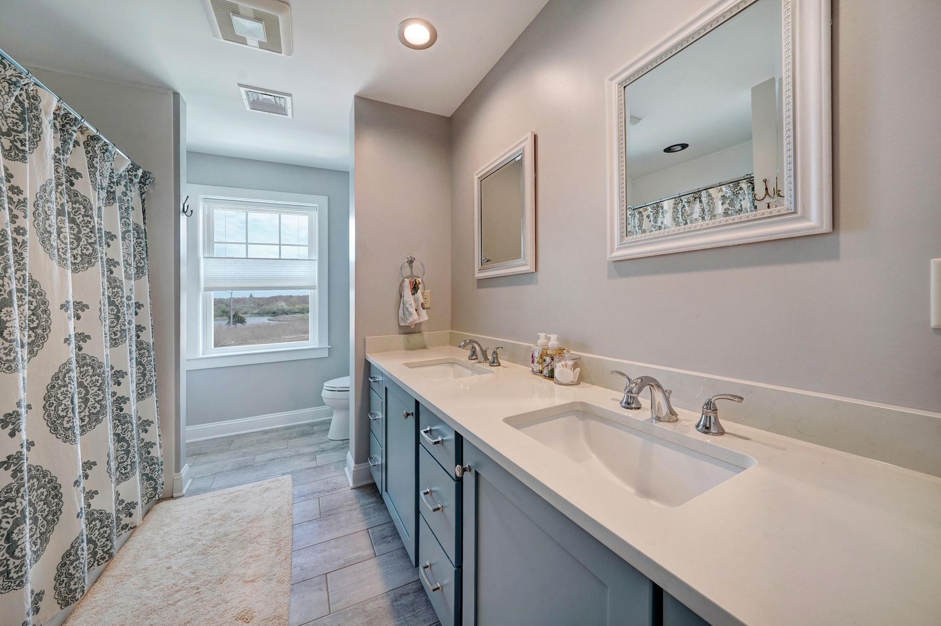 Bathroom with gray walls, blue vanity, and white fixtures. Shower curtain has a black and white pattern.