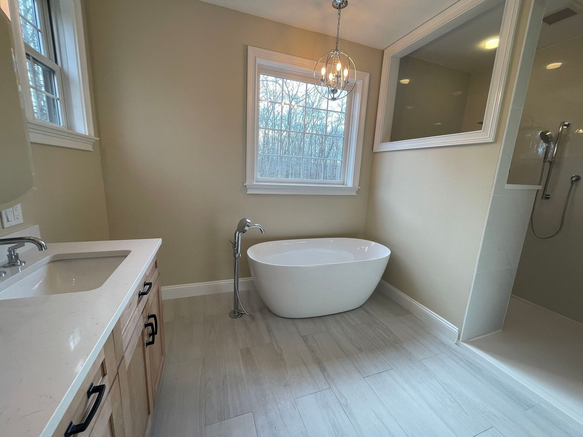 Bathroom with white soaking tub, marble-look floor, window, vanity, and glass shower.