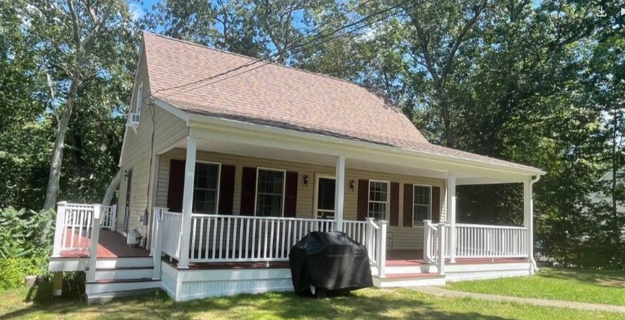 Tan house with a covered porch, white railing, and brown roof. A grill sits on the porch.