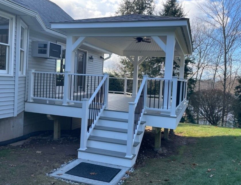 White deck with black railings and a gazebo-like roof. Steps lead down to a grassy yard.