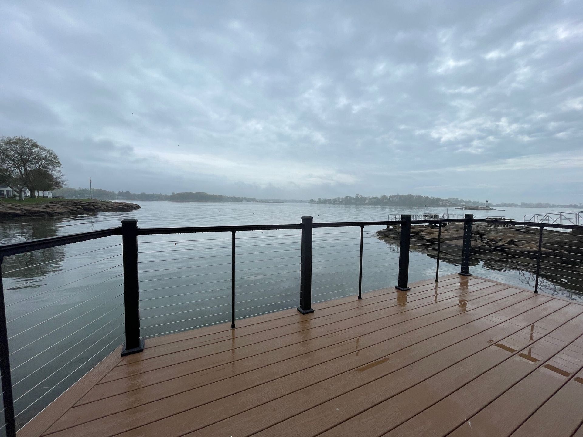 Wooden dock overlooking a gray, overcast body of water with a black railing.