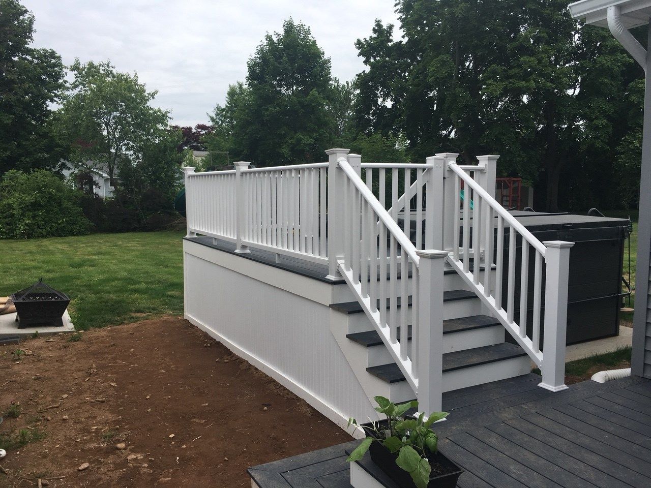 White deck with stairs and railing, adjacent to a hot tub, set in a backyard.