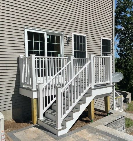 White deck with stairs, railing, and a sliding glass door against a gray house exterior.