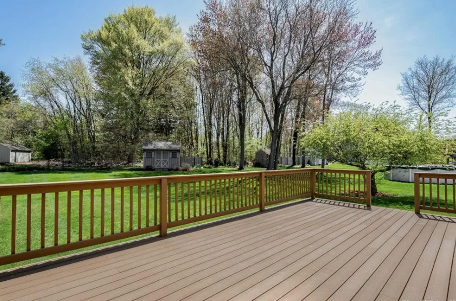 Wooden deck overlooking a grassy backyard with trees and a shed on a sunny day.