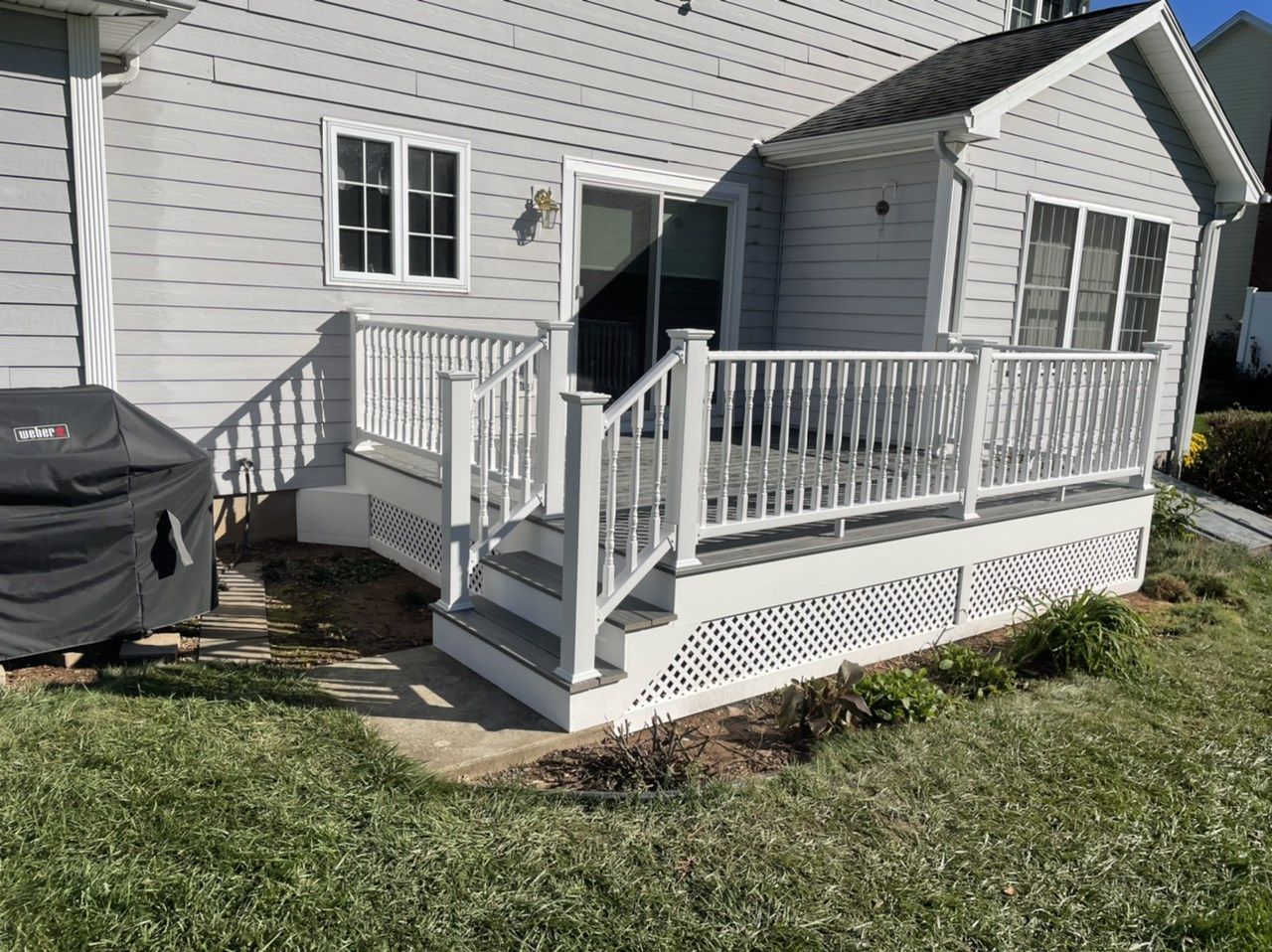 White deck with stairs, railing, and lattice, leading to a house with gray siding; a covered grill sits nearby.