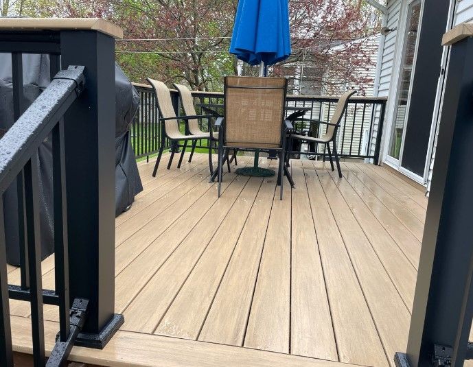 Wooden deck with black railing, table, and chairs under a blue umbrella.