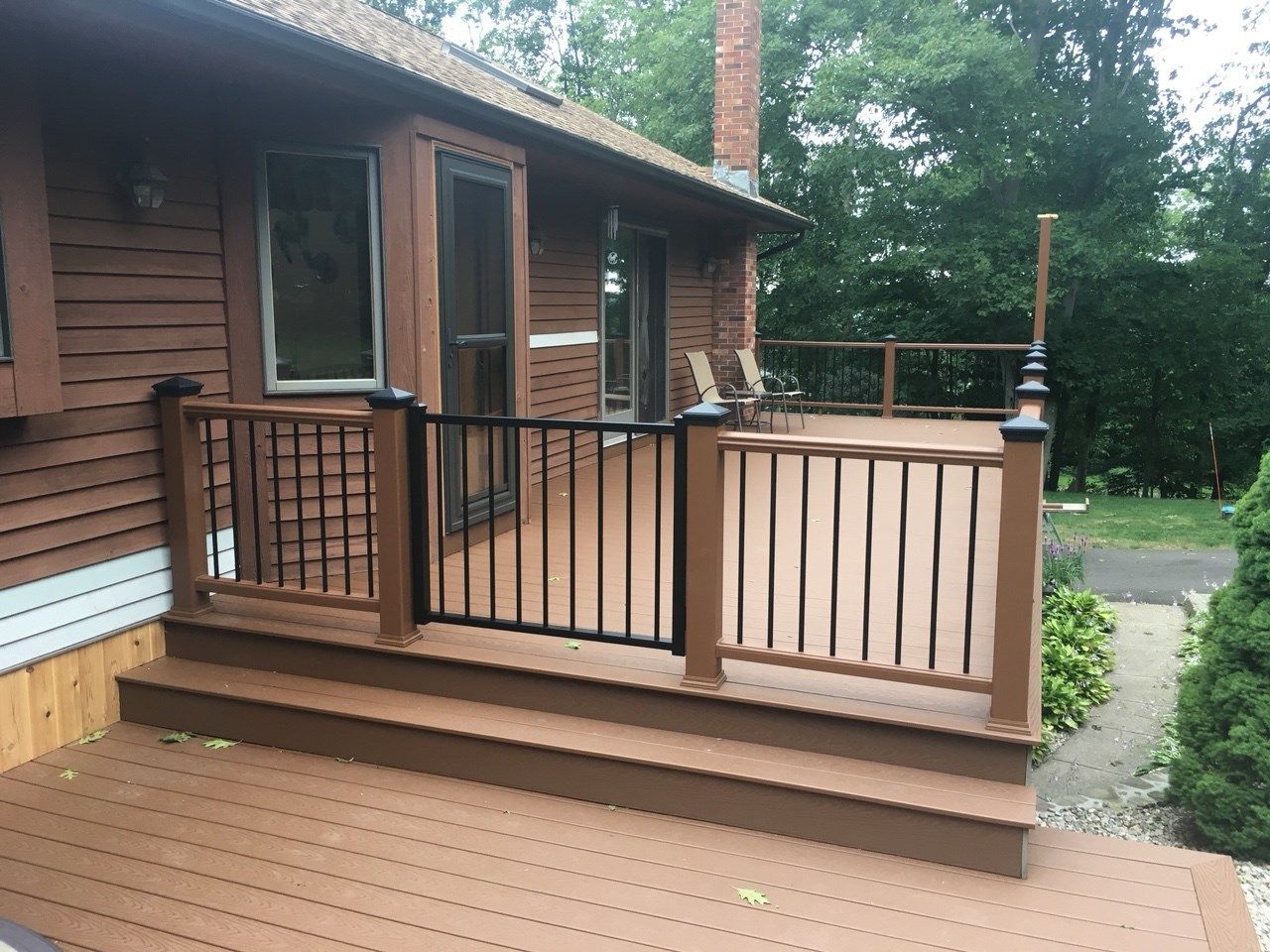 Brown deck with black railing and gate attached to a house.