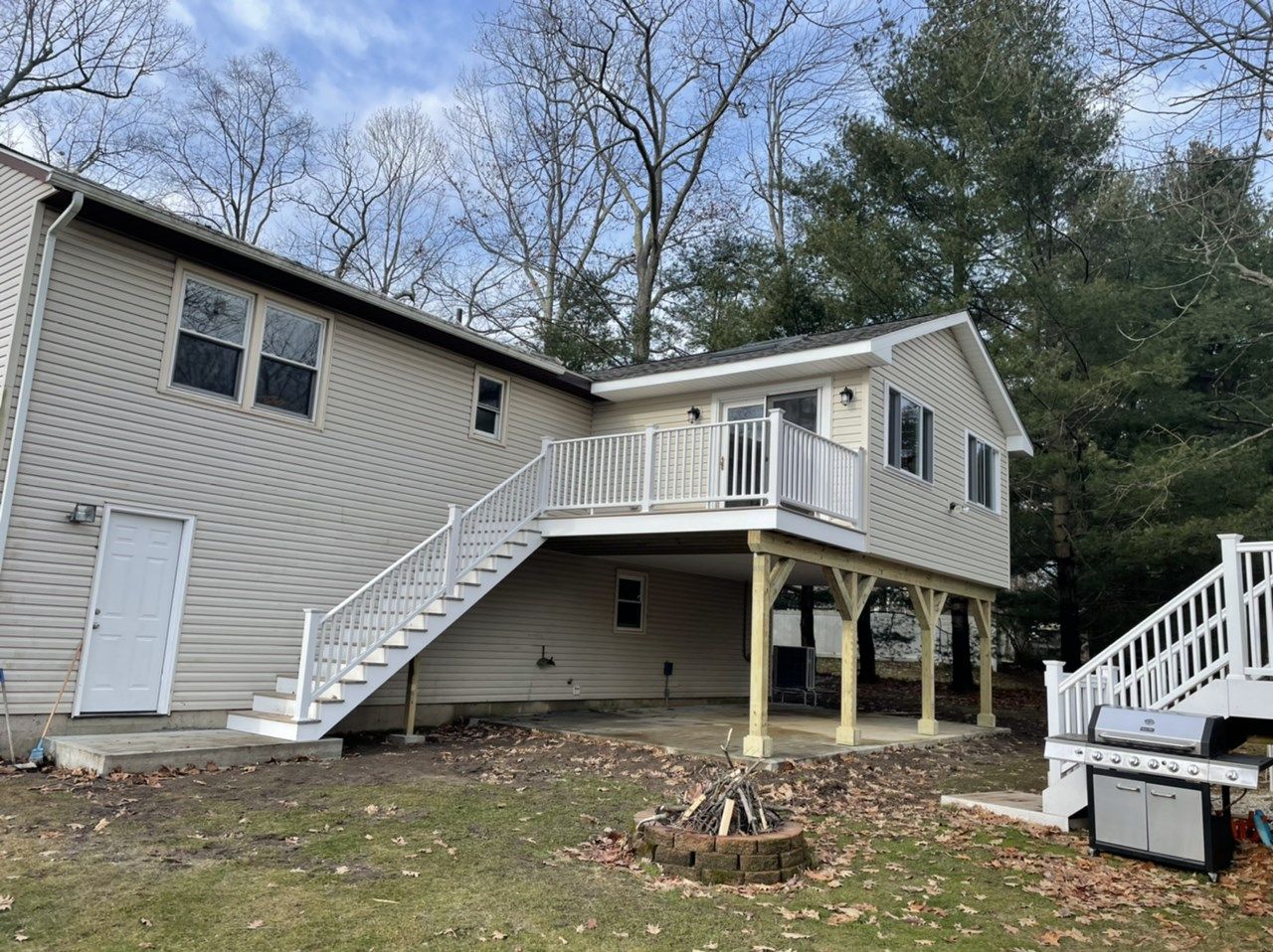 Back of a house with a multi-level deck, white railing, stairs, and beige siding.