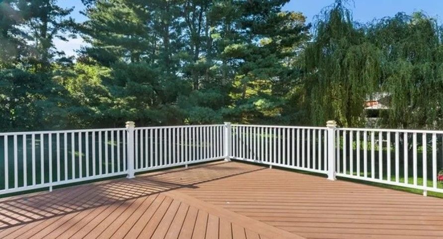 Wooden deck with white railing, surrounded by trees.
