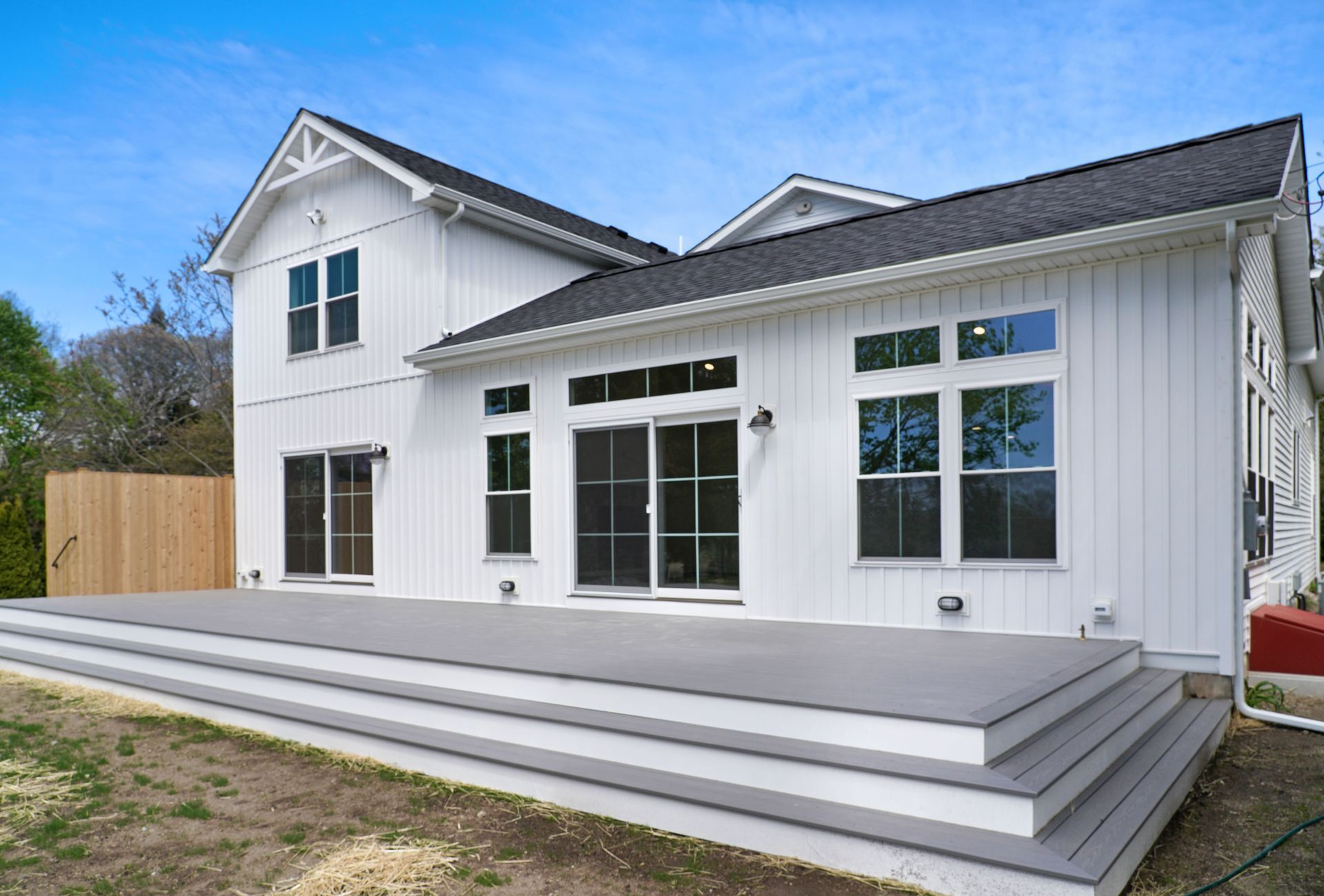 White house with gray deck. Sliding glass doors and windows, black roof, and light blue sky.