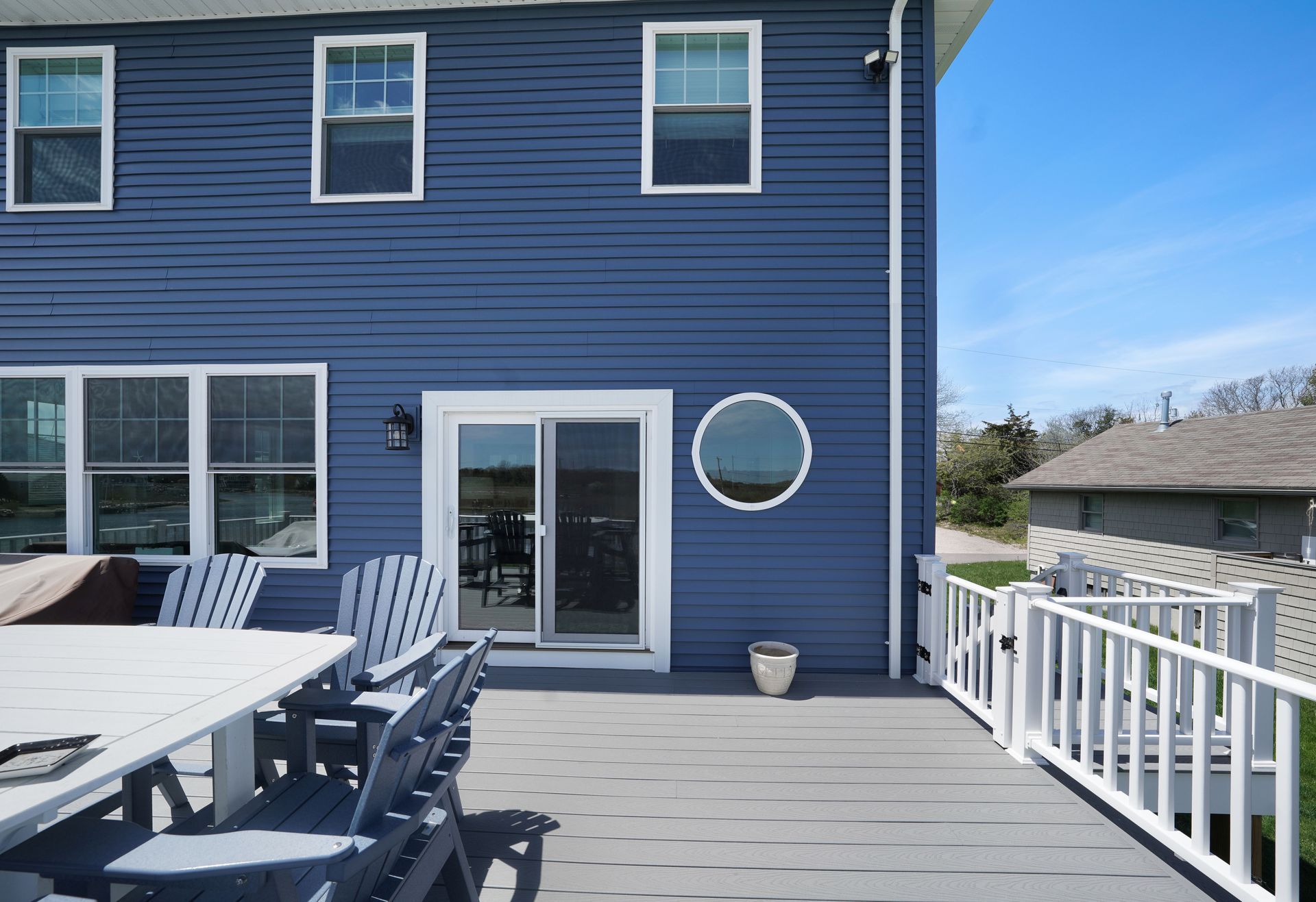 Blue house exterior with a deck, sliding door, round window, and white railing.