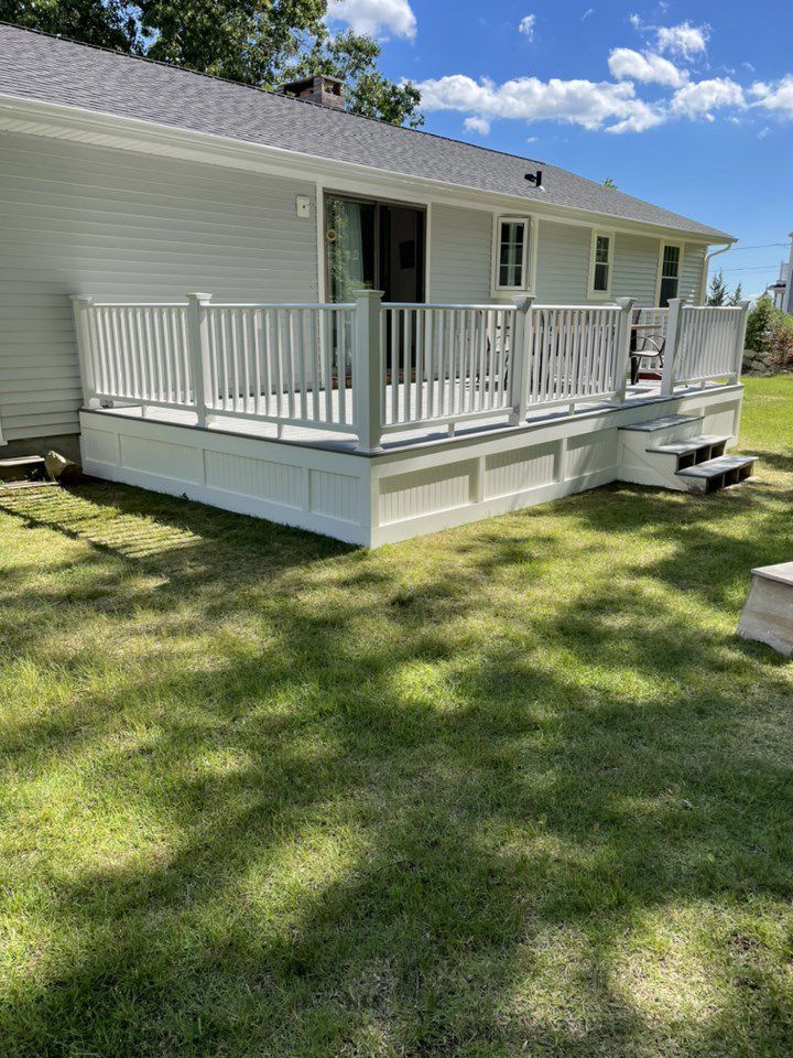 White deck attached to a house with steps leading to a grassy yard on a sunny day.