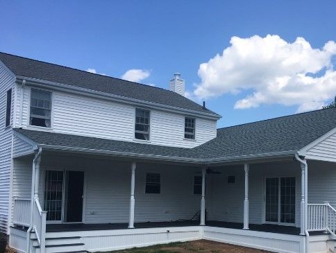 White two-story house with a porch. Gray roof, white trim. Blue sky with clouds.