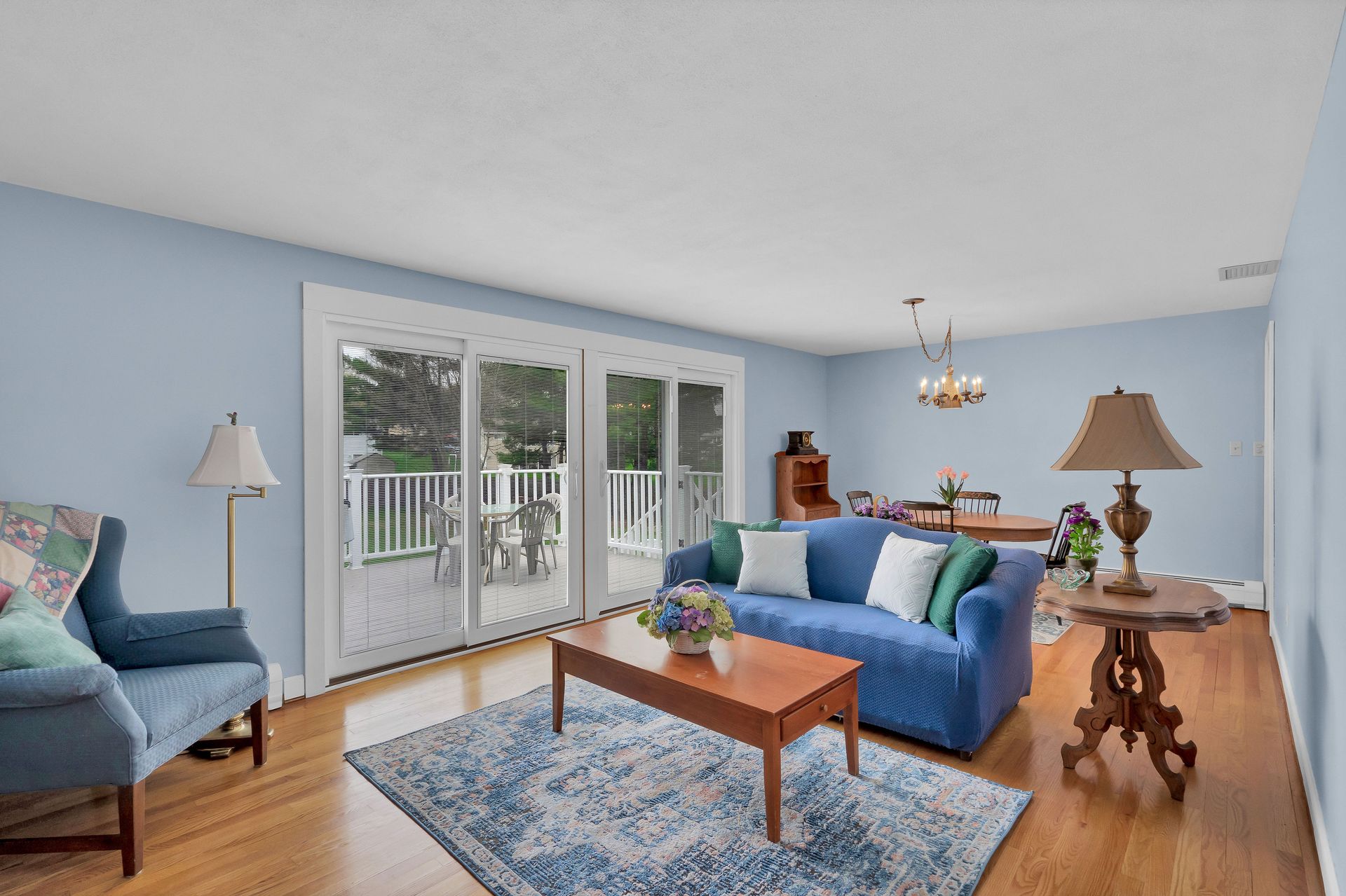 Living room with blue walls, hardwood floors, and sliding glass doors to a deck. Furnishings include a blue sofa and rug.