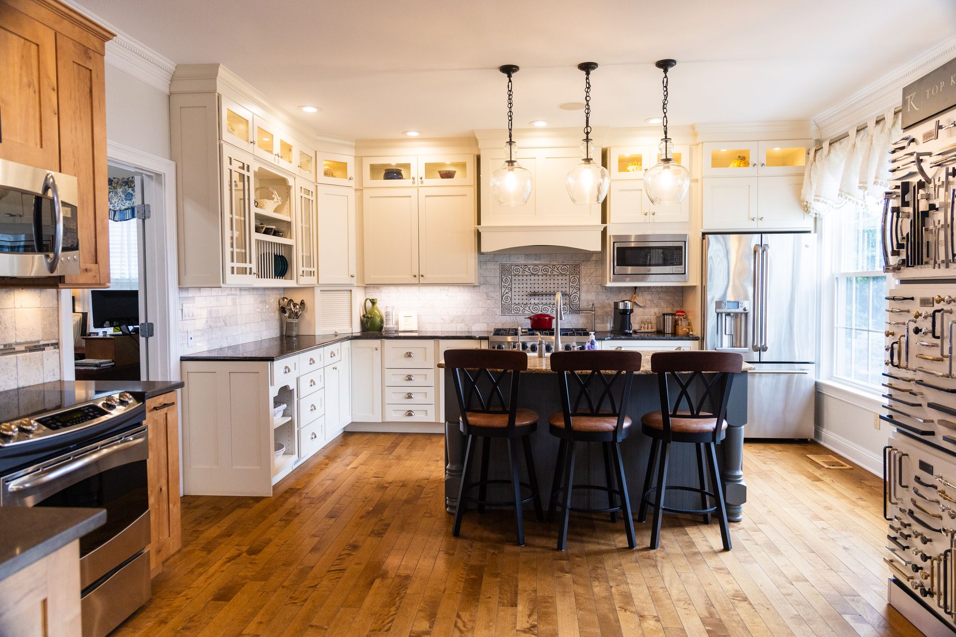 Kitchen with hardwood floors, white and wood cabinets, island with stools, and pendant lights.