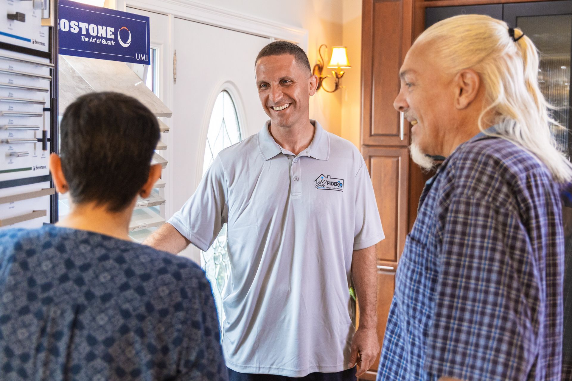 Three people in a home, discussing flooring options. Man in gray shirt smiles at two others.