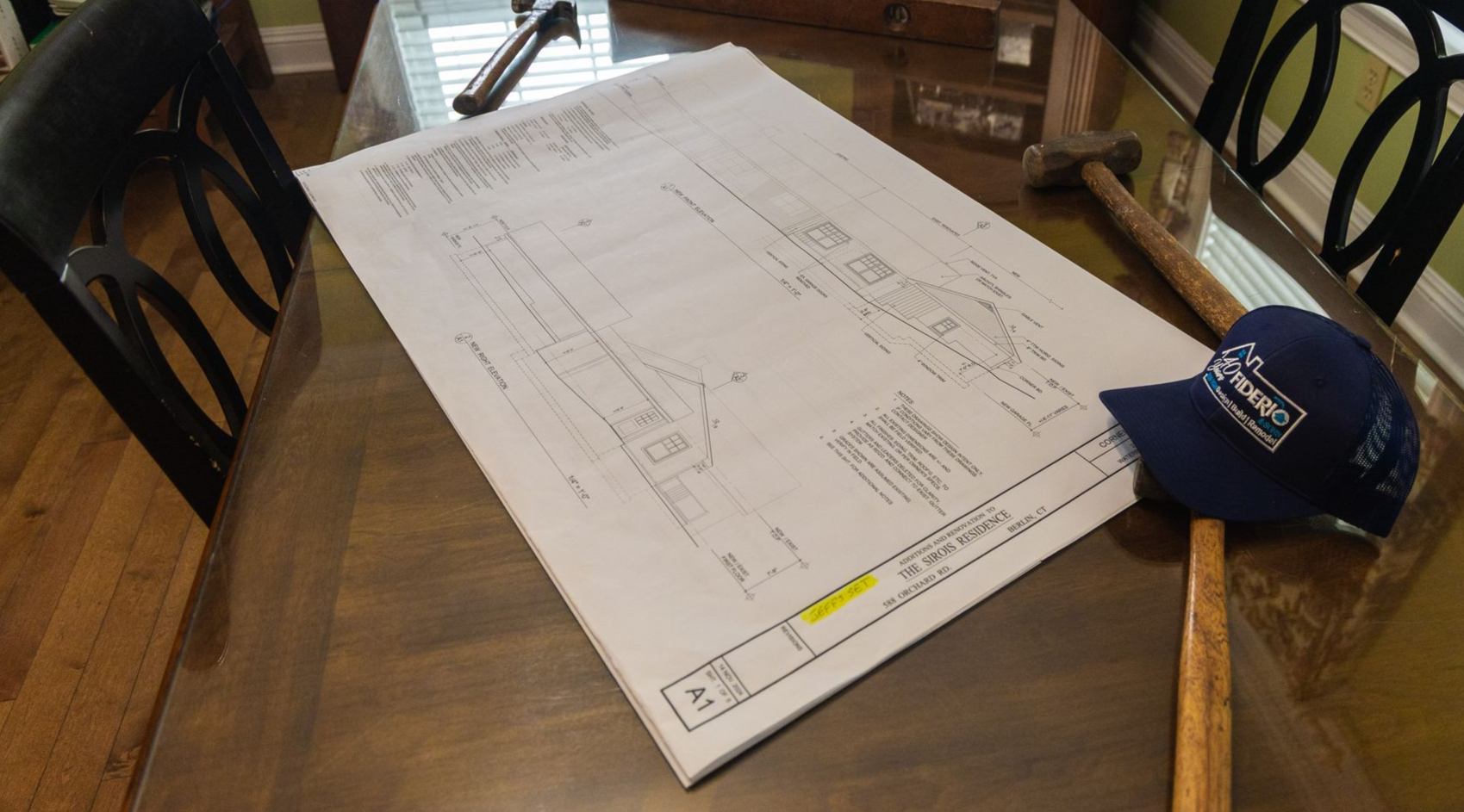 A blueprint and a hat rest on a wooden table, with tools.