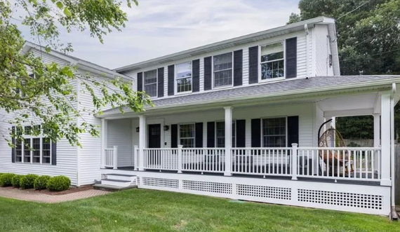 White two-story house with black shutters, a porch, and a green lawn.