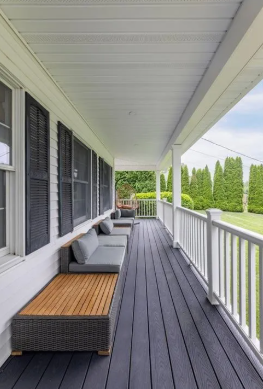 Covered porch with dark gray deck, white railing, outdoor seating, and shutters.