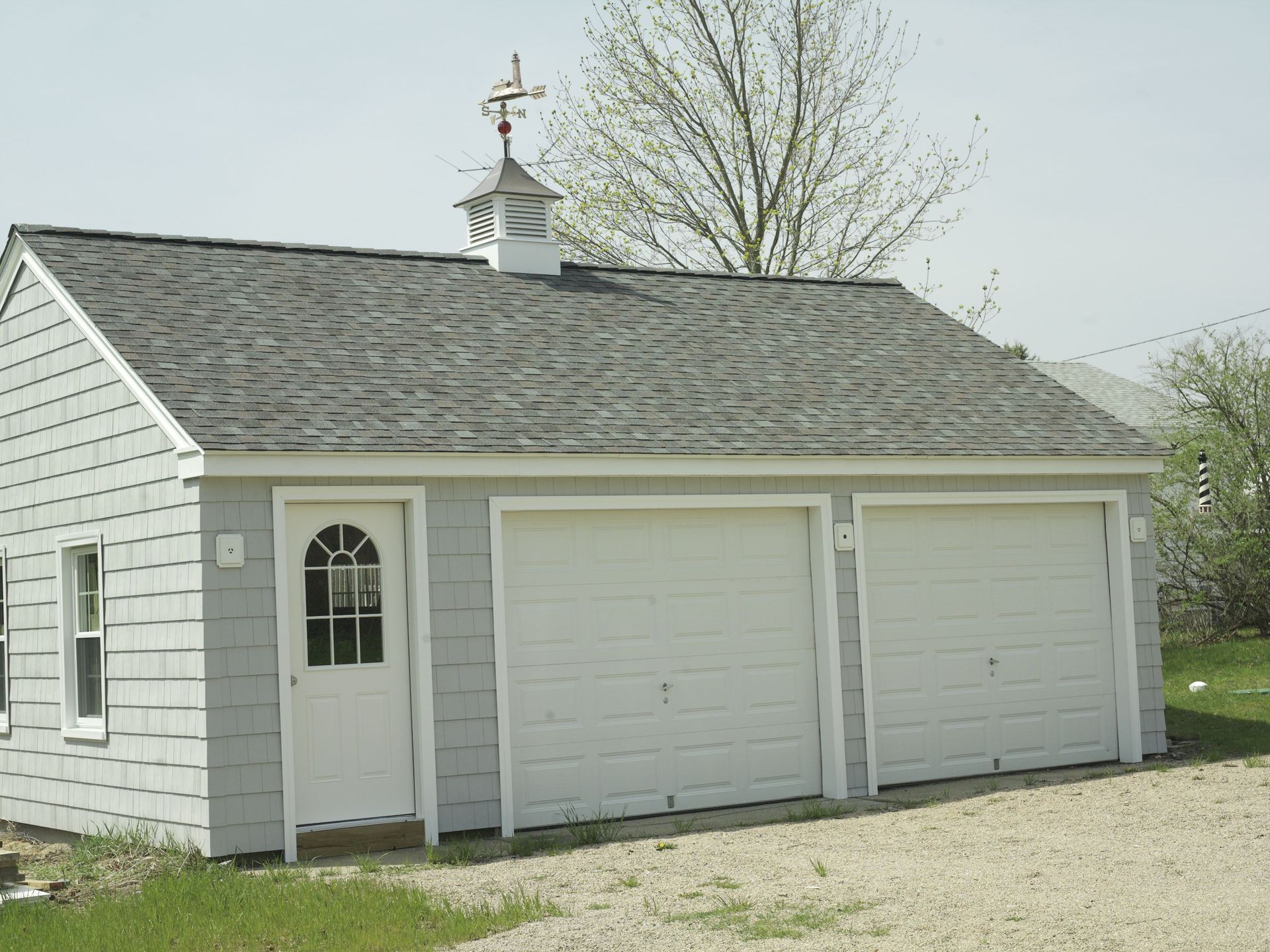 Light blue, two-car garage with white doors, a small door, and a weather vane on the roof.