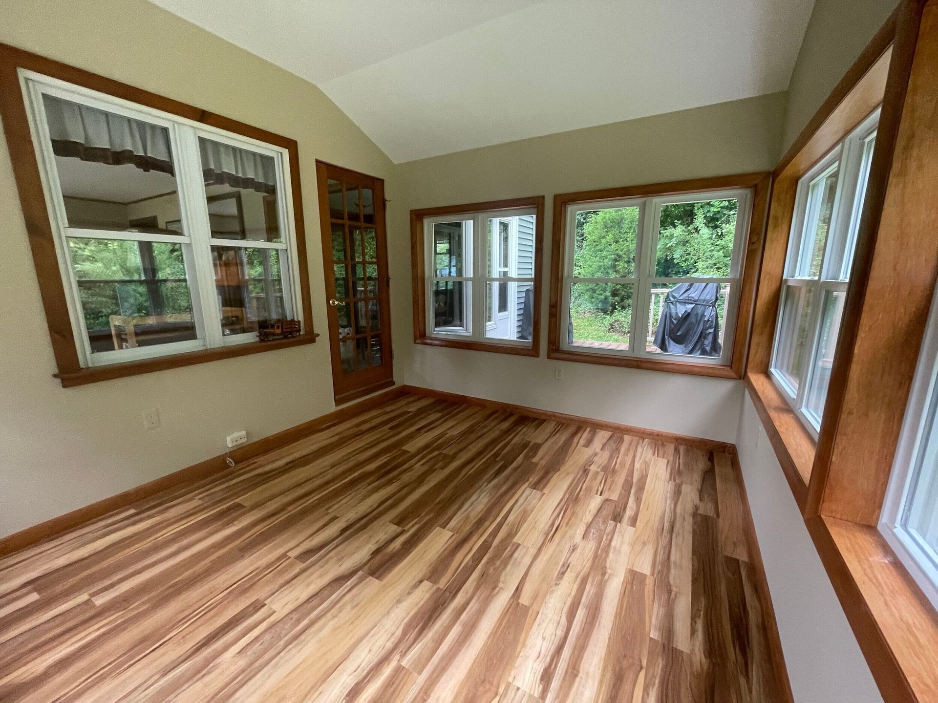 Sunroom with wood floors, windows with brown trim, beige walls, and a door.