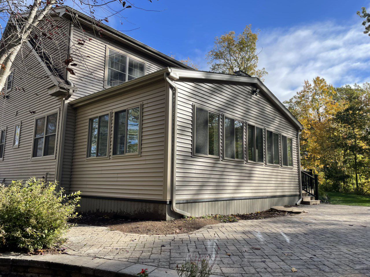 Beige house with a sunroom, surrounded by trees and a brick patio.