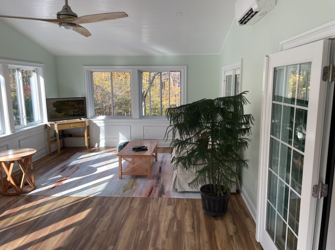 Sunroom with wood floors, light green walls, windows, French doors, and a ceiling fan.