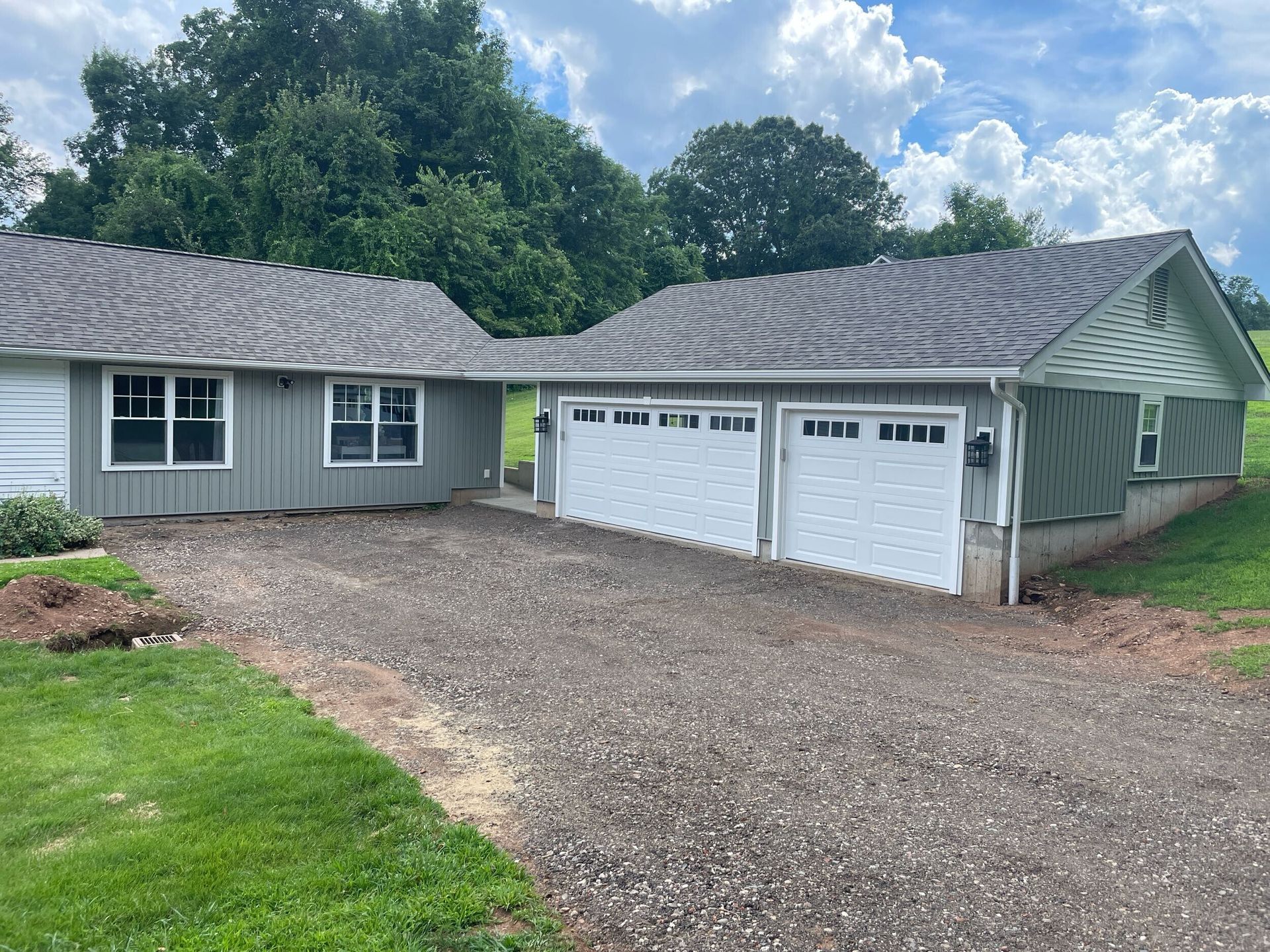 Gray house with two garage doors and gravel driveway.