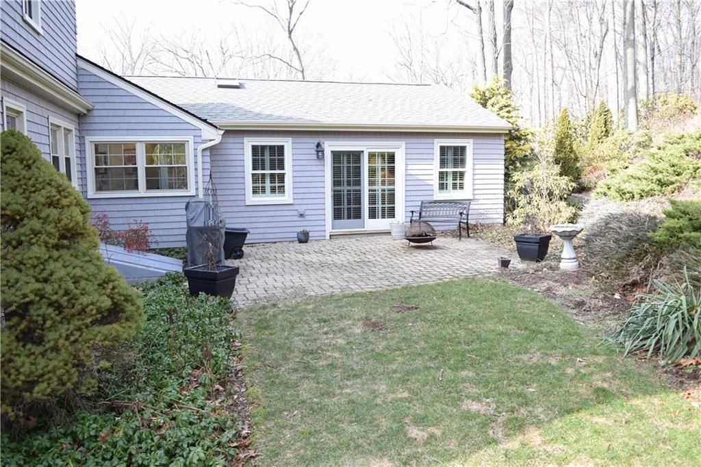 Backyard patio with sliding glass door, grey siding, brick pavers, and some bushes.
