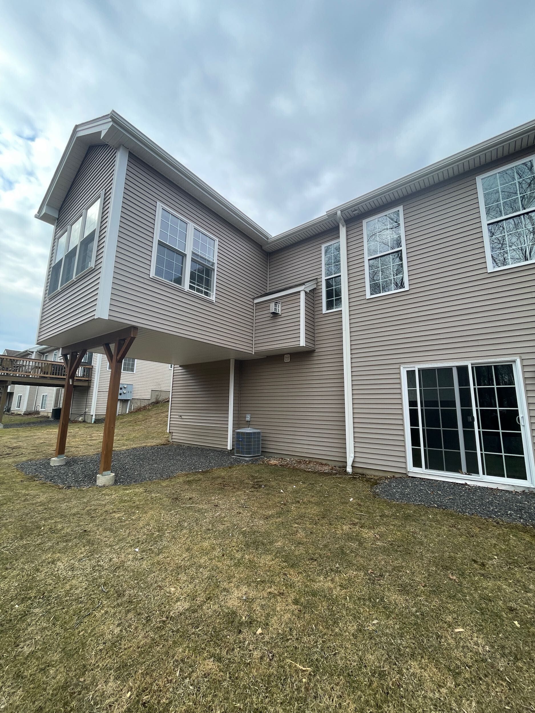 Exterior view of a two-story house with light brown siding, windows, and an elevated porch.