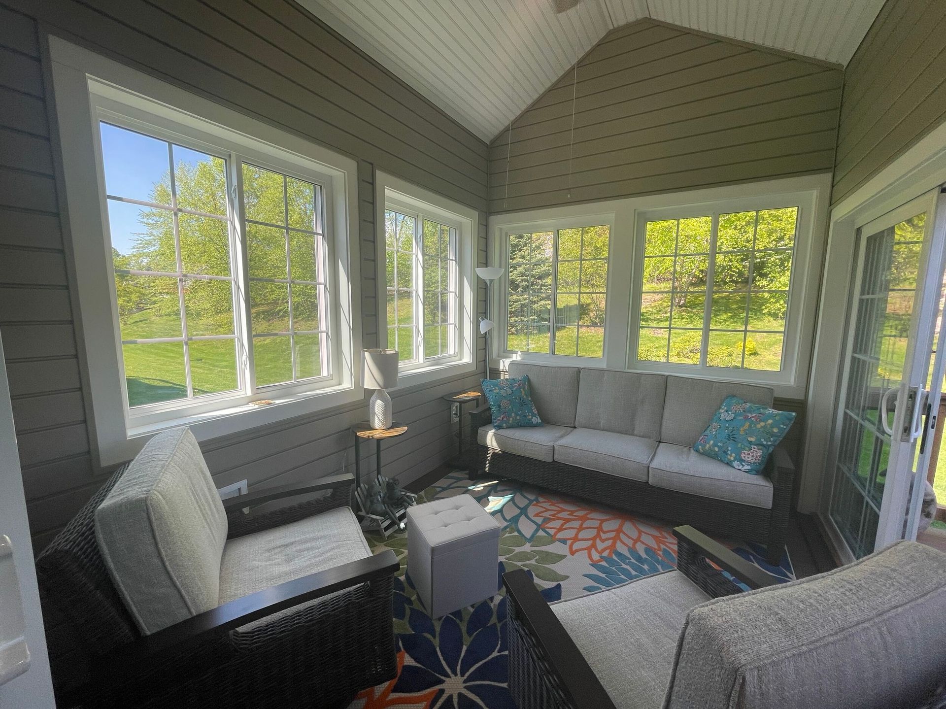 Sunroom with white-framed windows, wicker furniture, colorful rug, and a couch with blue pillows.