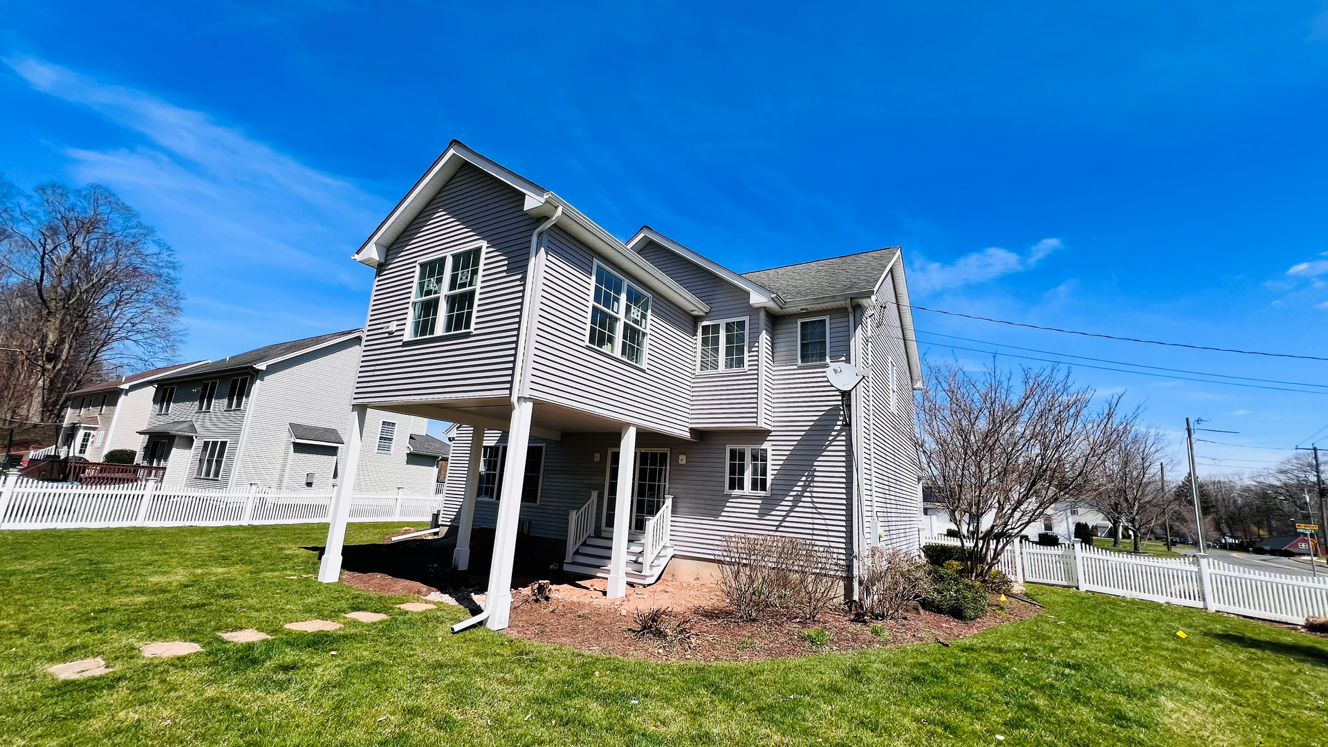 Two-story gray house with a porch, green lawn, white picket fence, and blue sky.