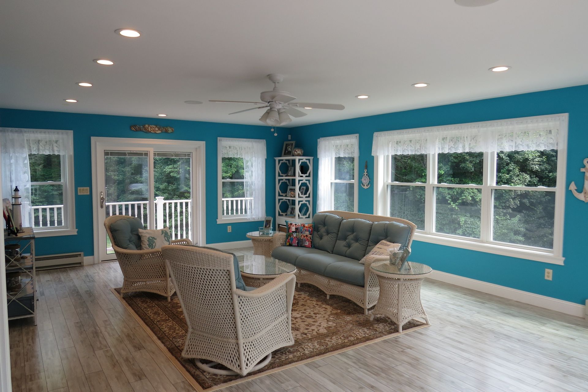 Bright blue living room with white wicker furniture, windows, and light wood floors.