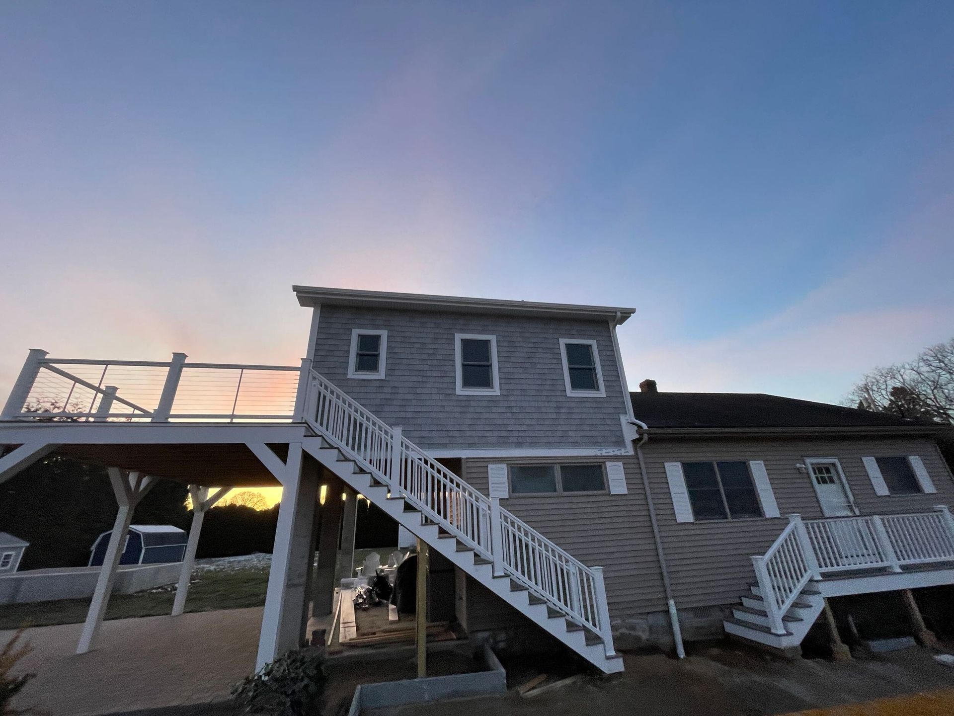 Two-story house with exterior stairs and deck against a sunset sky.