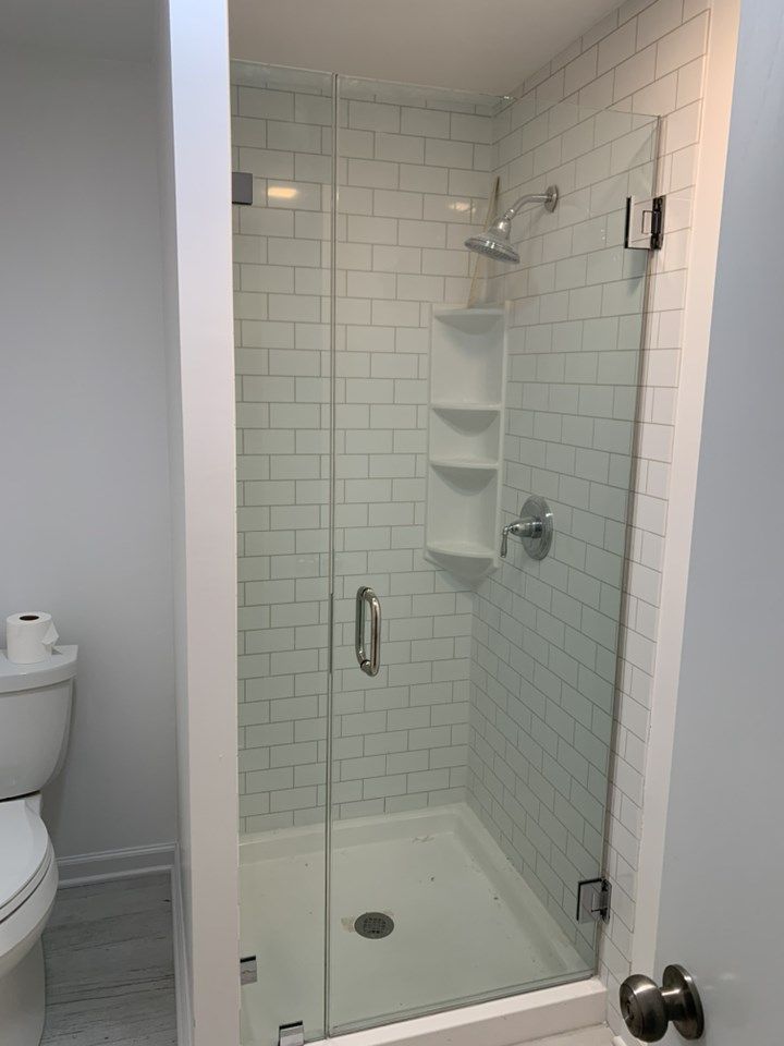 Glass-enclosed shower with white subway tile, a built-in shelf, and a chrome shower head and handle.